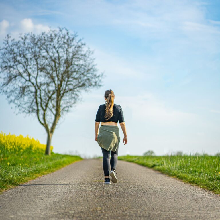 Mujer caminando por un sendero al aire libre bajo un cielo despejado